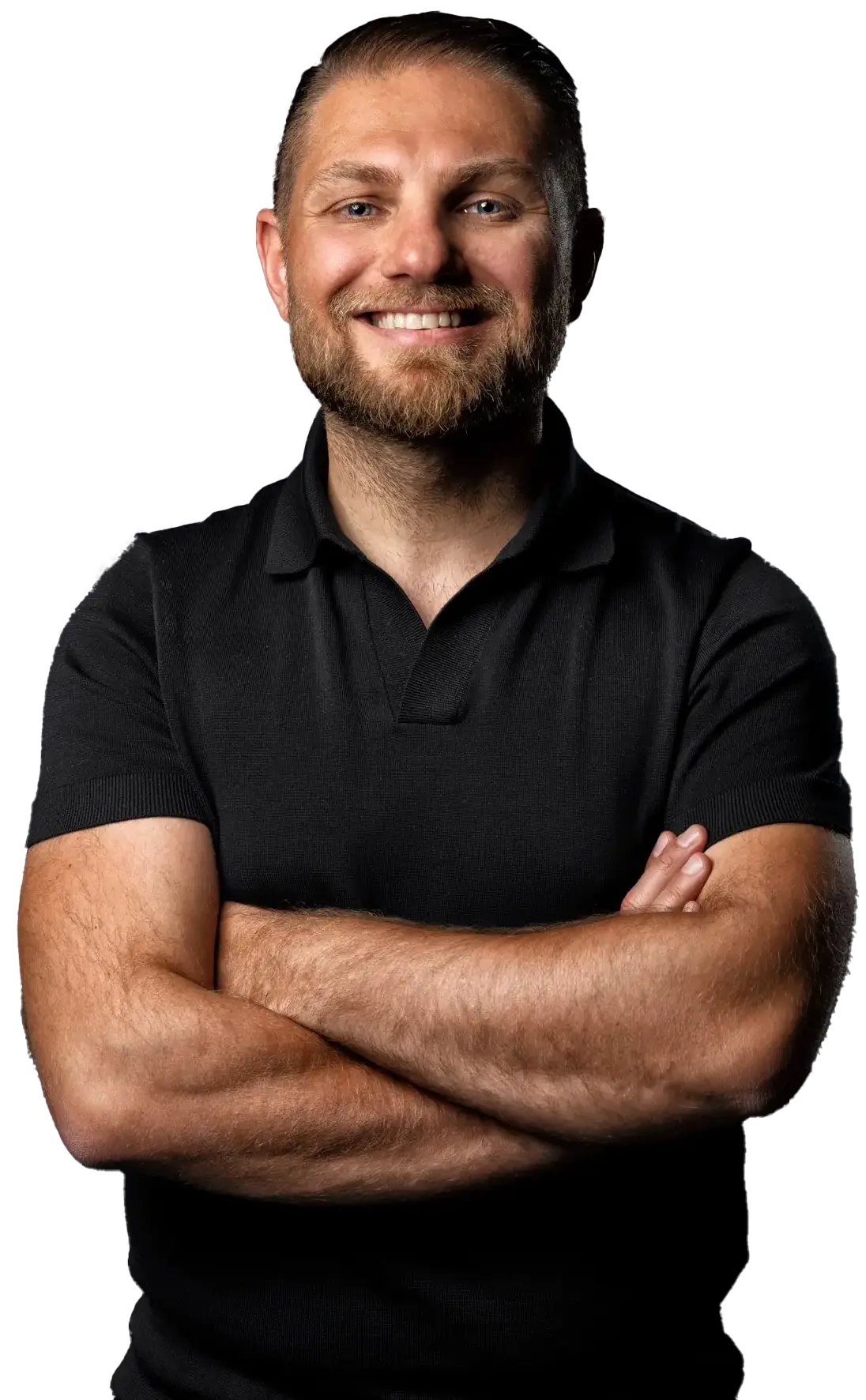 Man met baard en zwarte polo staat lachend met armen over elkaar tegen een donkere achtergrond.